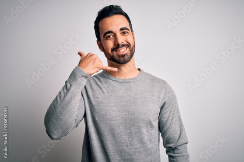 Young handsome man with beard wearing casual sweater standing over white background smiling doing phone gesture with hand and fingers like talking on the telephone. Communicating concepts.