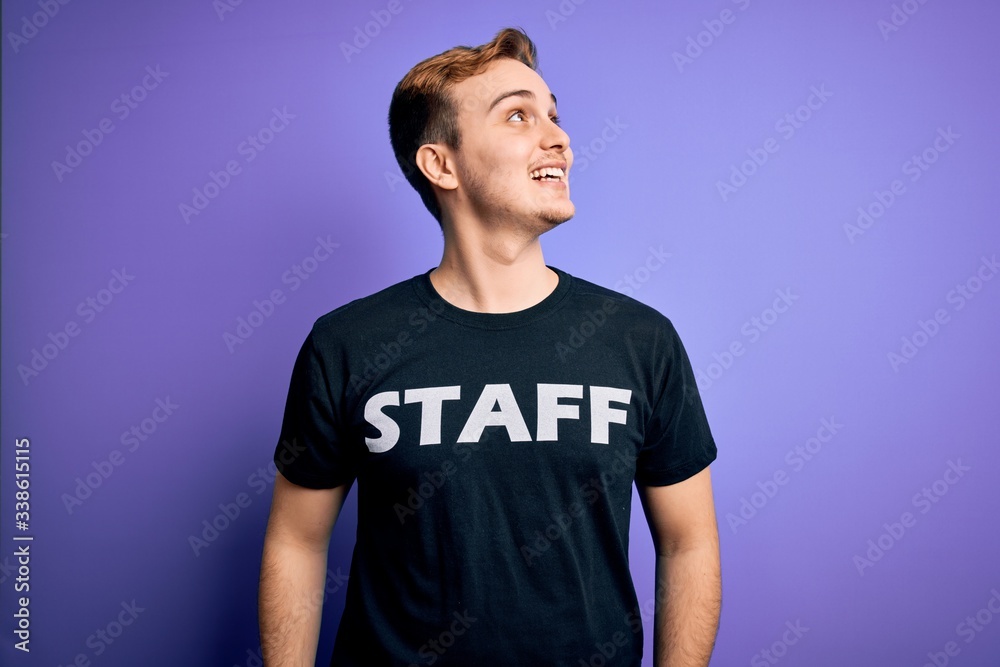 Young handsome redhead worker man wearing staff t-shirt uniform over purple background looking away to side with smile on face, natural expression. Laughing confident. Young handsome redhead worker man wearing staff t-shirt uniform over purple background looking away to side with smile on face, natural expression. Laughing confident.