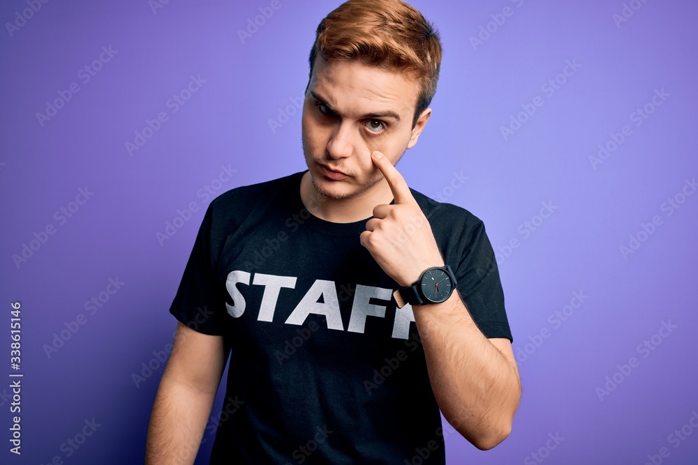 Young handsome redhead worker man wearing staff t-shirt uniform over purple background Pointing to the eye watching you gesture, suspicious expression Young handsome redhead worker man wearing staff t-shirt uniform over purple background Pointing to the eye watching you gesture, suspicious expression