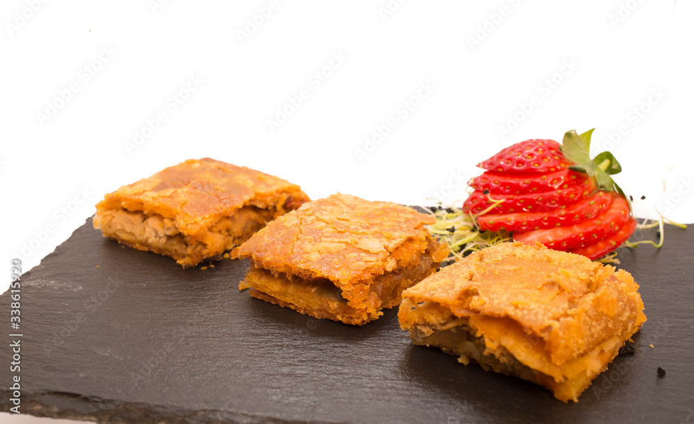 Pieces of Galician pie on slate plate decorated with strawberries on white background