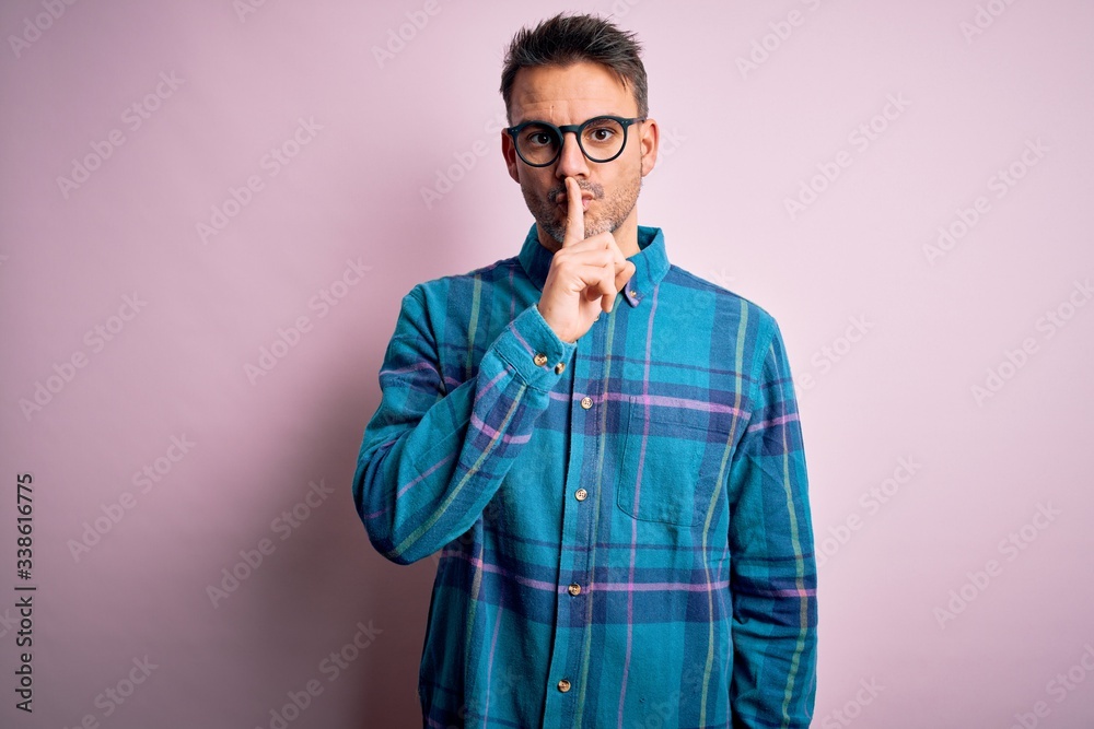 Young handsome man wearing casual shirt and glasses standing over isolated pink background asking to be quiet with finger on lips. Silence and secret concept. Young handsome man wearing casual shirt and glasses standing over isolated pink background asking to be quiet with finger on lips. Silence and secret concept.