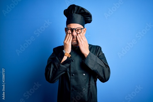 Young handsome chef man wearing cooker uniform and hat over isolated blue background rubbing eyes for fatigue and headache, sleepy and tired expression. Vision problem