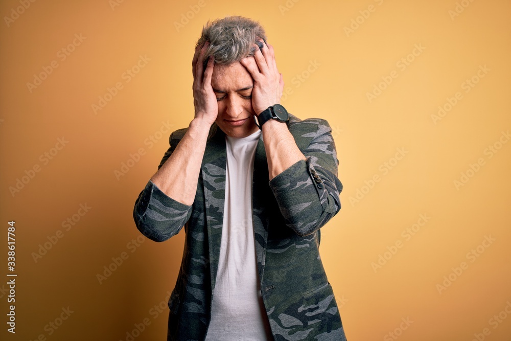 Young handsome modern man wearing business jacket standing over yellow isolated background suffering from headache desperate and stressed because pain and migraine. Hands on head. Young handsome modern man wearing business jacket standing over yellow isolated background suffering from headache desperate and stressed because pain and migraine. Hands on head.