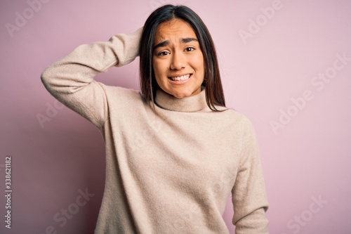 Young beautiful asian woman wearing casual turtleneck sweater over pink background confuse and wonder about question. Uncertain with doubt, thinking with hand on head. Pensive concept. © Krakenimages.com