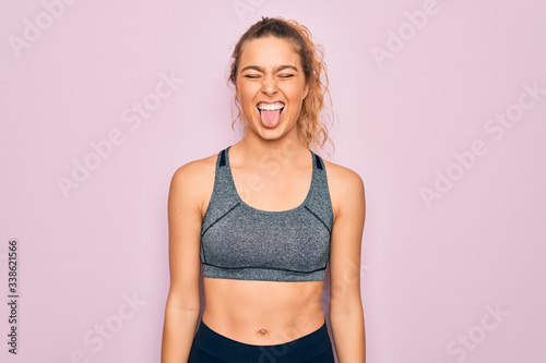 Young beautiful blonde sportswoman with blue eyes doing exercise wearing sportswear sticking tongue out happy with funny expression. Emotion concept.