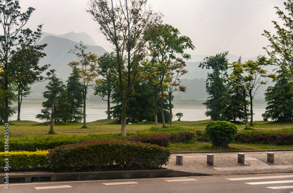 Chenjiawan, China - May 5, 2010: Green park along Yangtze River with shape of mountains under foggy silver sky as backdrop. Street up front. Chenjiawan, China - May 5, 2010: Green park along Yangtze River with shape of mountains under foggy silver sky as backdrop. Street up front.