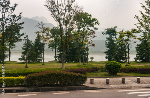 Chenjiawan, China - May 5, 2010: Green park along Yangtze River with shape of mountains under foggy silver sky as backdrop. Street up front.