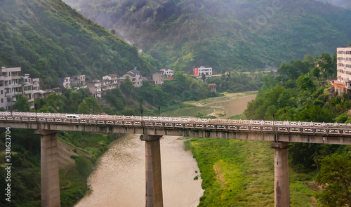 Yichang, China - May 5, 2010: Bridge on pillars over brown meandering rivers between green mountain slopes with houses along a road.