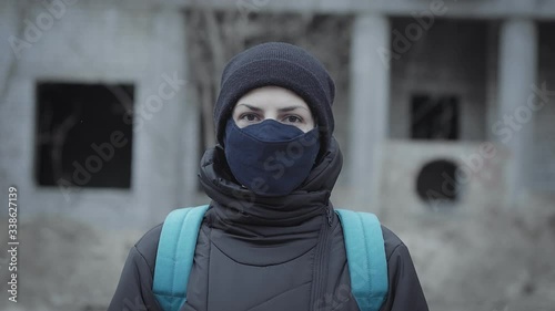 Portrait of a young woman in a protective mask against the background of an abandoned building in an industrial post-apocalyptic landscape. Pandemic protection, air pollution