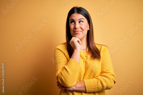 Young beautiful woman wearing casual sweater over yellow isolated background with hand on chin thinking about question, pensive expression. Smiling with thoughtful face. Doubt concept.