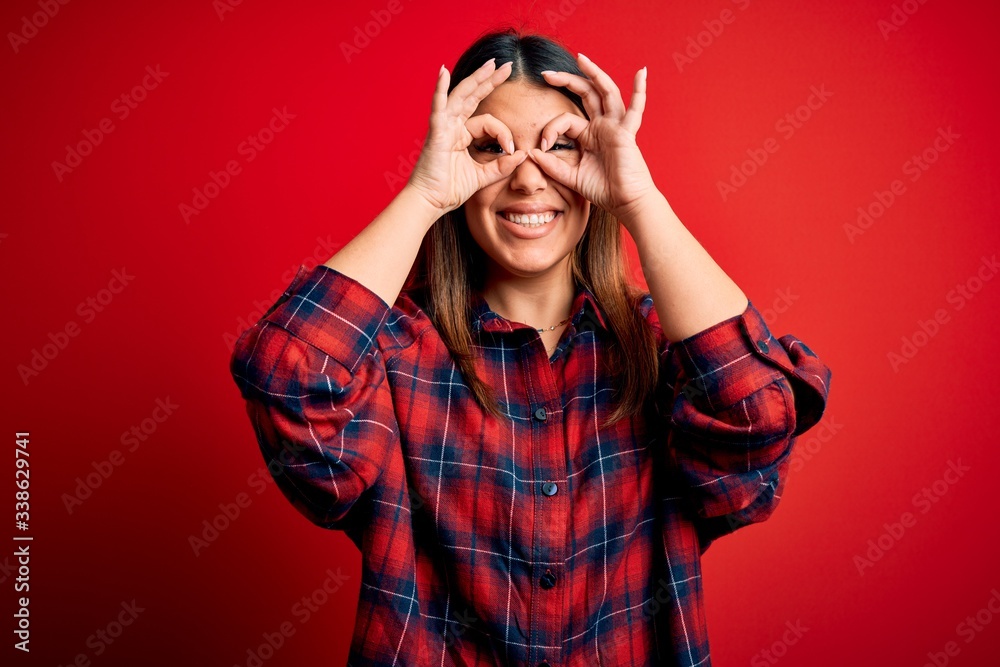 Young beautiful woman wearing casual shirt over red background doing ok gesture like binoculars sticking tongue out, eyes looking through fingers. Crazy expression. Young beautiful woman wearing casual shirt over red background doing ok gesture like binoculars sticking tongue out, eyes looking through fingers. Crazy expression.
