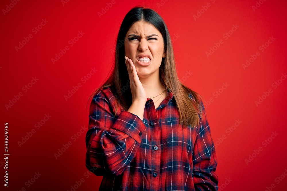 Young beautiful woman wearing casual shirt over red background touching mouth with hand with painful expression because of toothache or dental illness on teeth. Dentist Young beautiful woman wearing casual shirt over red background touching mouth with hand with painful expression because of toothache or dental illness on teeth. Dentist
