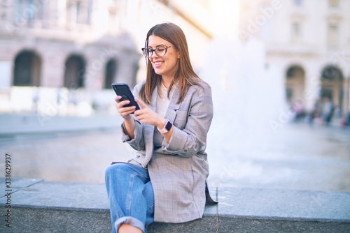 Young beautiful woman smiling happy and confident. Sitting with smile on face using smartphone at the city