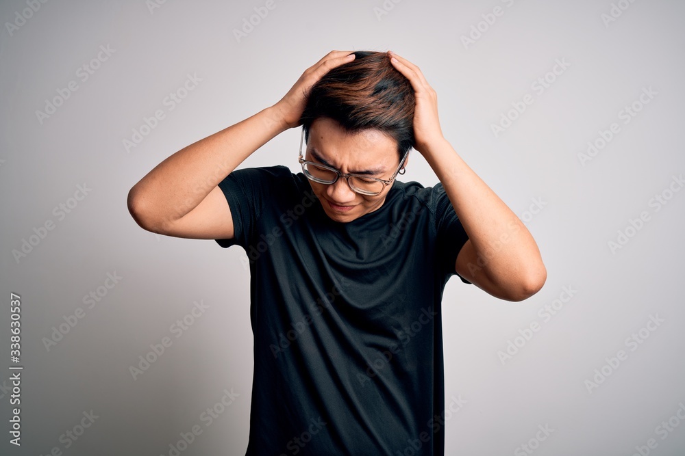Young handsome chinese man wearing black t-shirt and glasses over white background suffering from headache desperate and stressed because pain and migraine. Hands on head. Young handsome chinese man wearing black t-shirt and glasses over white background suffering from headache desperate and stressed because pain and migraine. Hands on head.