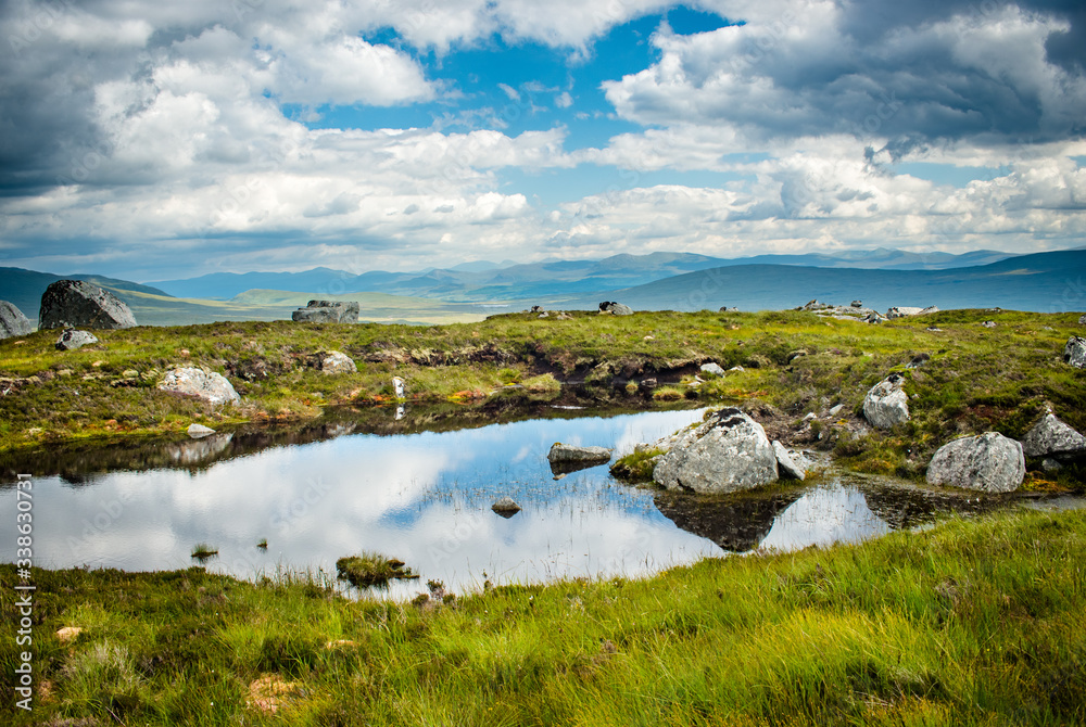 Clouds reflect in pond on top of hill in the Scottish Highlands