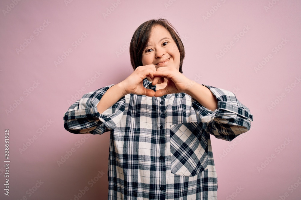 Young down syndrome woman wearing casual shirt over pink background smiling in love showing heart symbol and shape with hands. Romantic concept. Young down syndrome woman wearing casual shirt over pink background smiling in love showing heart symbol and shape with hands. Romantic concept.