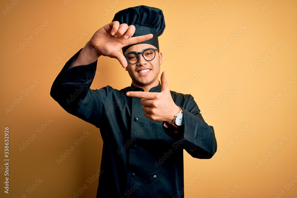 Young brazilian chef man wearing cooker uniform and hat over isolated yellow background smiling making frame with hands and fingers with happy face. Creativity and photography concept. Young brazilian chef man wearing cooker uniform and hat over isolated yellow background smiling making frame with hands and fingers with happy face. Creativity and photography concept.