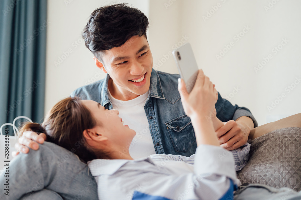 Obraz premium Young Asian couple at home using a smartphone