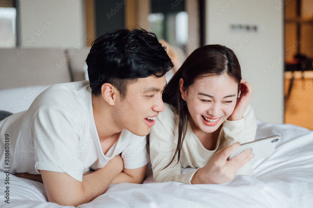 Fototapeta premium Young Asian couple at home using a smartphone