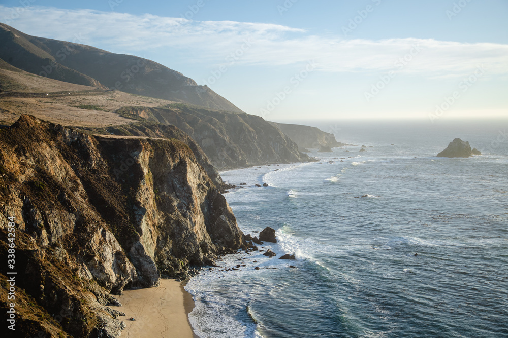 Aerial drone view of the Big Sur coastline in California. Beautiful golden light hitting the side of the cliffs at sunset along the coastal road.