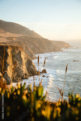 Aerial drone view of the Big Sur coastline in California. Beautiful golden light hitting the side of the cliffs at sunset along the coastal road.