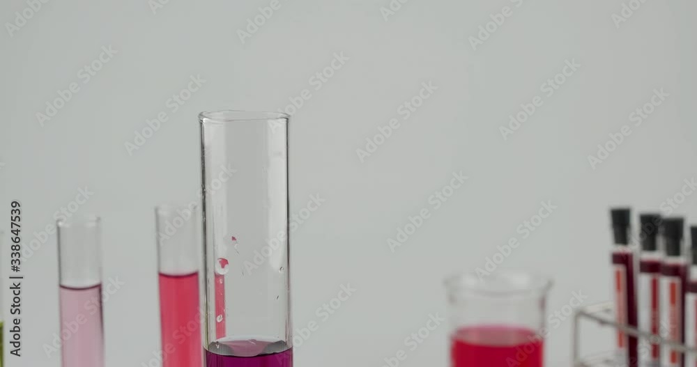 Slow motion truck shot of researcher wearing blue glove pouring green to purple clearly science liquid in to the test tube Slow motion truck shot of researcher wearing blue glove pouring green to purple clearly science liquid in to the test tube