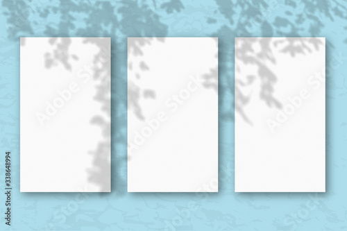 3 vertical sheets of white textured paper on a pastel blue wall background. Mockup with an overlay of plant shadows. Natural light casts shadows from the tree's foliage