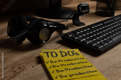 Home office theme: close-up.
To-do list to be productive with headband, microphone and computer on wooden desk. Productivity concept for online work. concept of avoiding distractions at home.