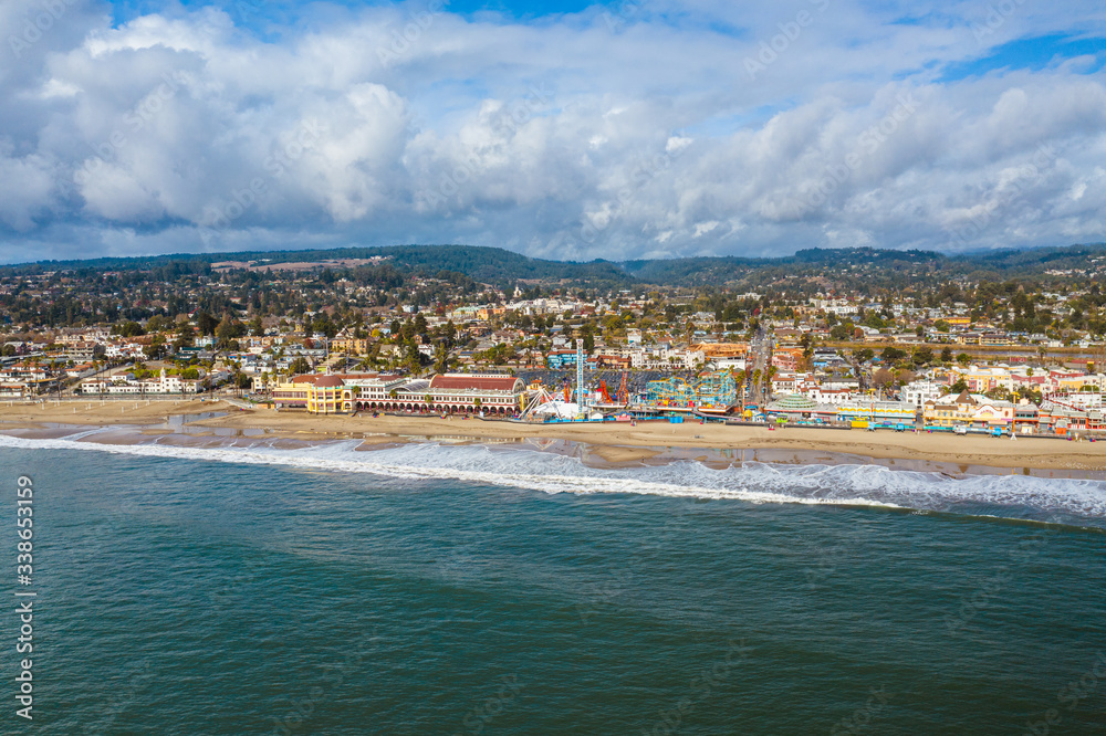 Aerial drone shot of Santa Cruz Beach Boardwalk. The colorful amusement park is next to the beach with mountains in the background. 