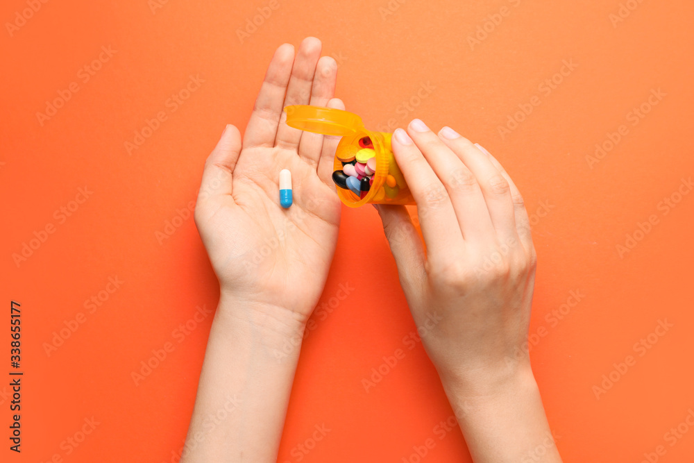Fototapeta premium Female hands with bottle and pills on color background