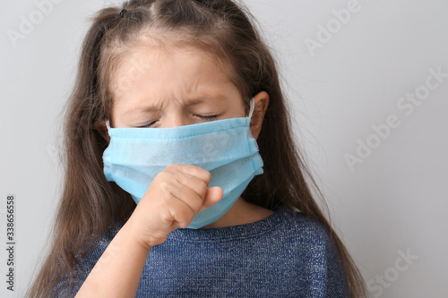 Sick little girl in protective medical mask on grey background