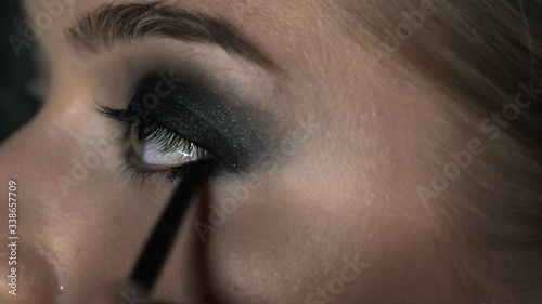 Macro shot of makeup artist making professional make-up for young woman in beauty studio. Make up Artist makes the makeup smokey eyes of a black shade with special brush of a beautiful model