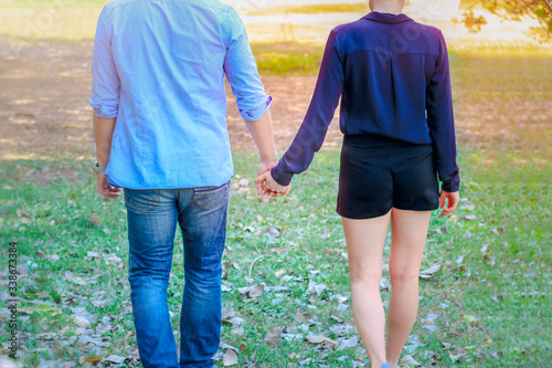 Sweet couple holding hands while relaxing and walking in park, young beautiful lover spending time together and having romantic moment in summer garden, love and romantic date concept