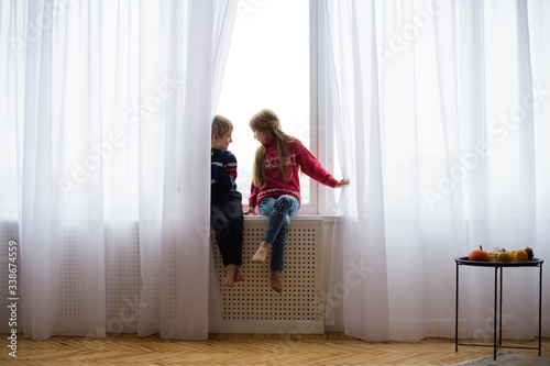 brother and sister are sitting on windowsill, near window glass, they want to walk on street, but in world there is  coronavirus pandemic, and they remain at home