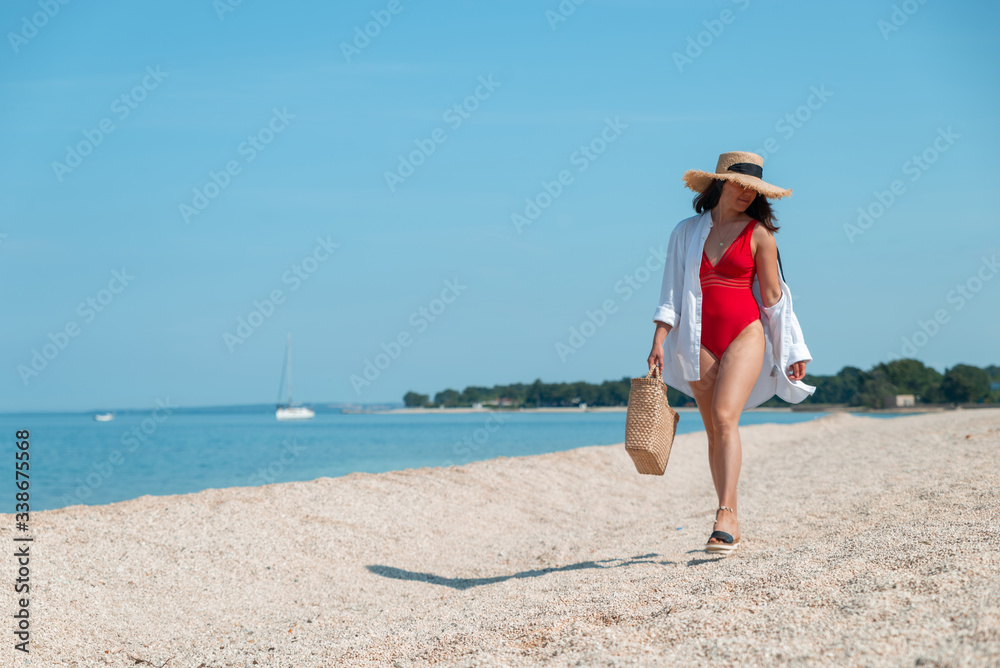 young stunning woman in red swimsuit walking by sea beach