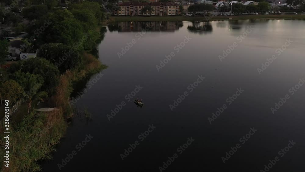 Slow aerial pull back and reveal two men in a fishing boat on a suburban city lake at sunset, South Florida