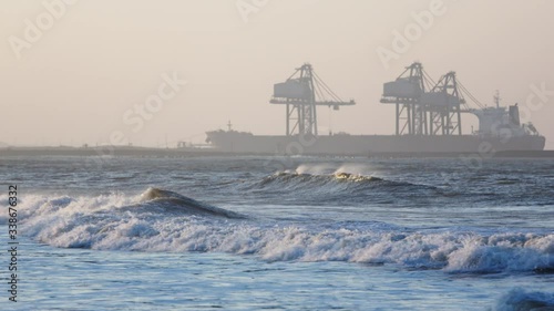 Cinematic Slow Motion Shot of Waves Rolling into Shore During Sunset With Cargo Ship at Container Crane at Port Talbot, Wales photo