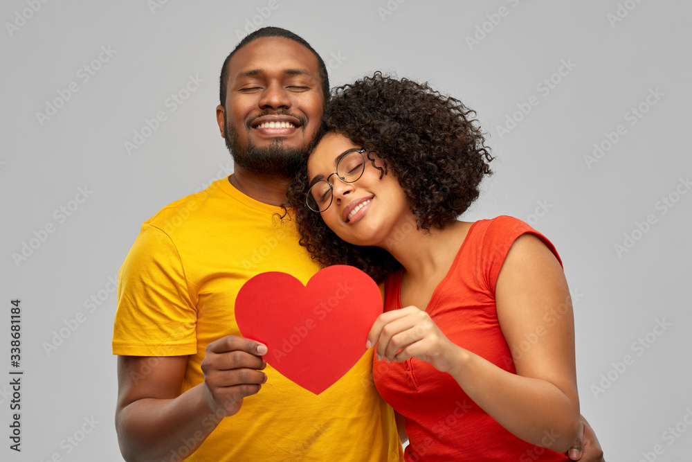 love, relationships and valentines day concept - happy african american couple holding big red paper heart over grey background