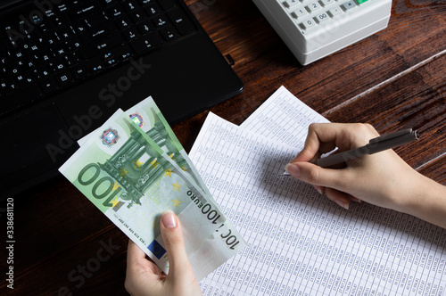 Obligation to pay wages and debts in the company.A cashier holds money Euro over an office work space with documents, a cash register,a phone,and a computer.Work in the office with finances in Europe photo