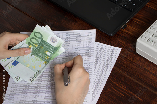 Work in the office with finance. A cashier holds money Euro over an office workspace with documents,a cash register, a phone, and a computer.Obligation to pay wages and debts in the company in Europe photo