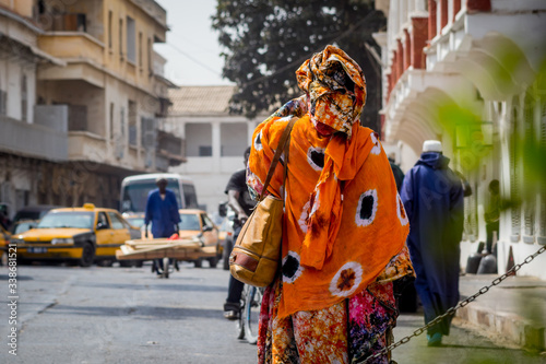 Back view of a typical african woman dressed in colorful  orange clothing on the streets of Sant Louis, Senegal during midday. photo