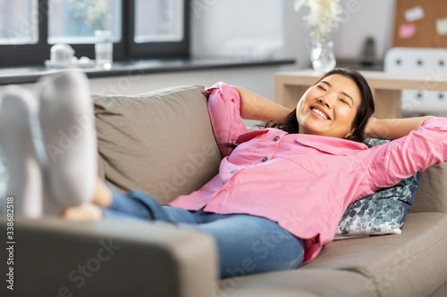 people and leisure concept - happy smiling asian young woman in pink shirt lying on sofa and dreaming at home