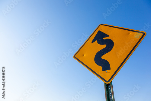 A curved road caution sign, blue sky with copy space
