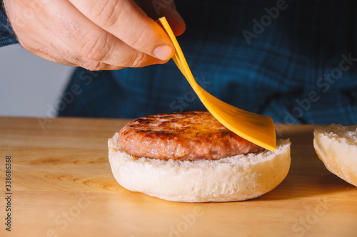 Man hands putting on top of a burger a slice of cheese on a wooden board. Cooking concept.