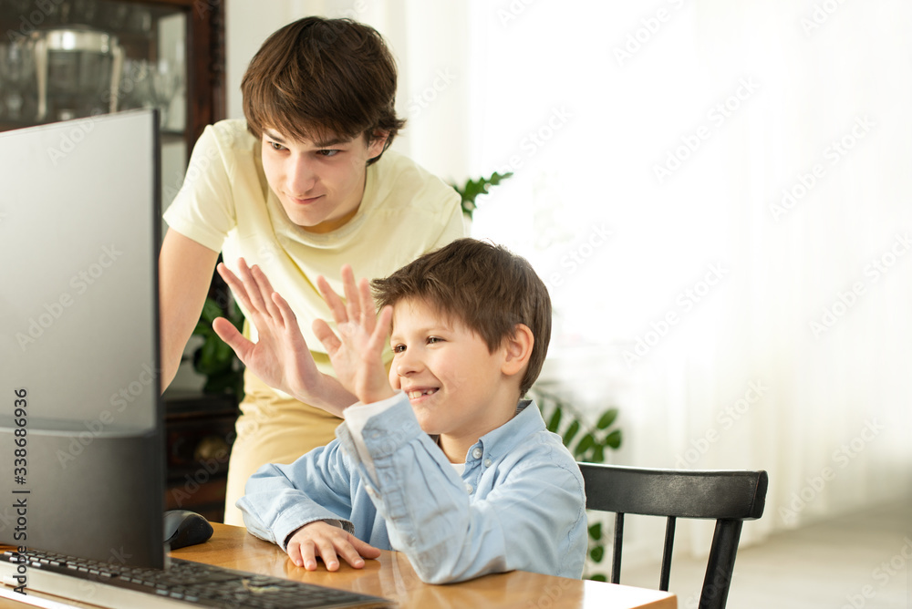 Smiling boy and teenager chatting online and waving at the computer screen. Quarantine and self-isolation due to coronavirus. Smiling boy and teenager chatting online and waving at the computer screen. Quarantine and self-isolation due to coronavirus.