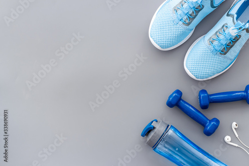 Sport background with sneakers and dumbbells on grey table top view copy space
