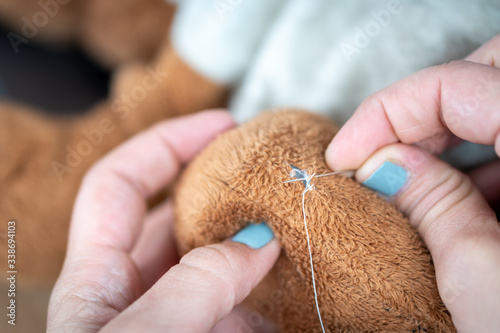 Quadro em tela Female hand with blue nail polish sewing a ripped and dirty teddy bear