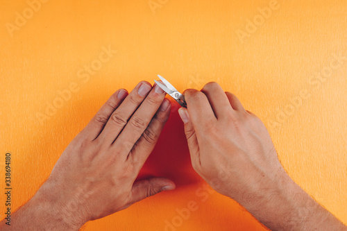 Fototapeta Top view man clipping fingernails on orange background