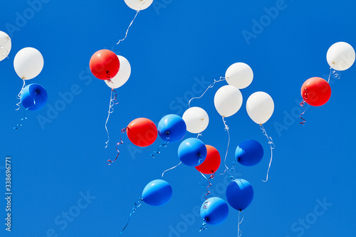 Multicolored helium balloons flying up in the blue sky