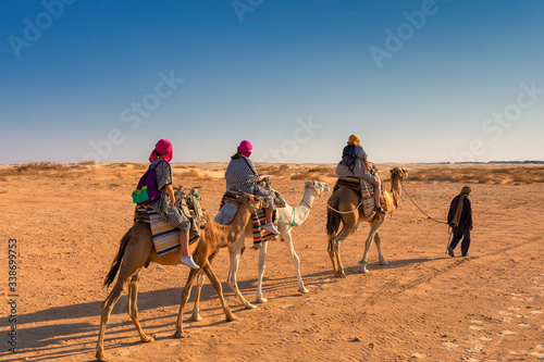 three people in Berber national robes on camel guided camels